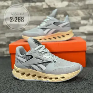 Zapatillas Reebok grises de malla con suela beige de diseño geométrico. Se muestran sobre una caja naranja. Tallas disponibles 37 al 40.